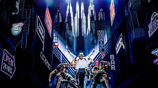 Myles Frost in the role of Michael Jackson is dancing on stage while wearing a black and white suit and the iconic hat.