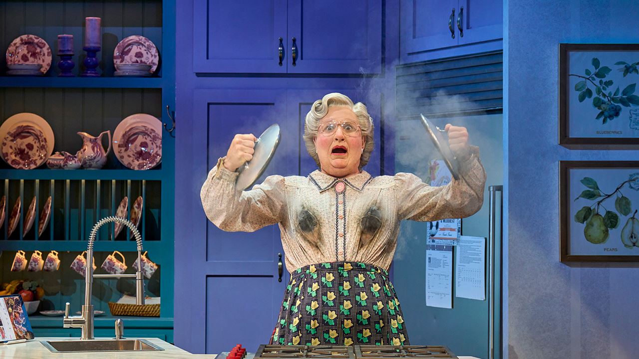 Laugh the night away at Mrs Doubtfire at the Shaftesbury Theatre. Image courtesy of See Tickets. Scottish nanny mrs doubtfire stands on stage holding two pot lids with a smoking bosom.