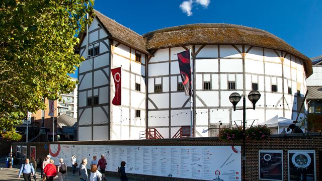 A photo of The Globe theatre taken on a sunny day, with blue sky above the theatre.