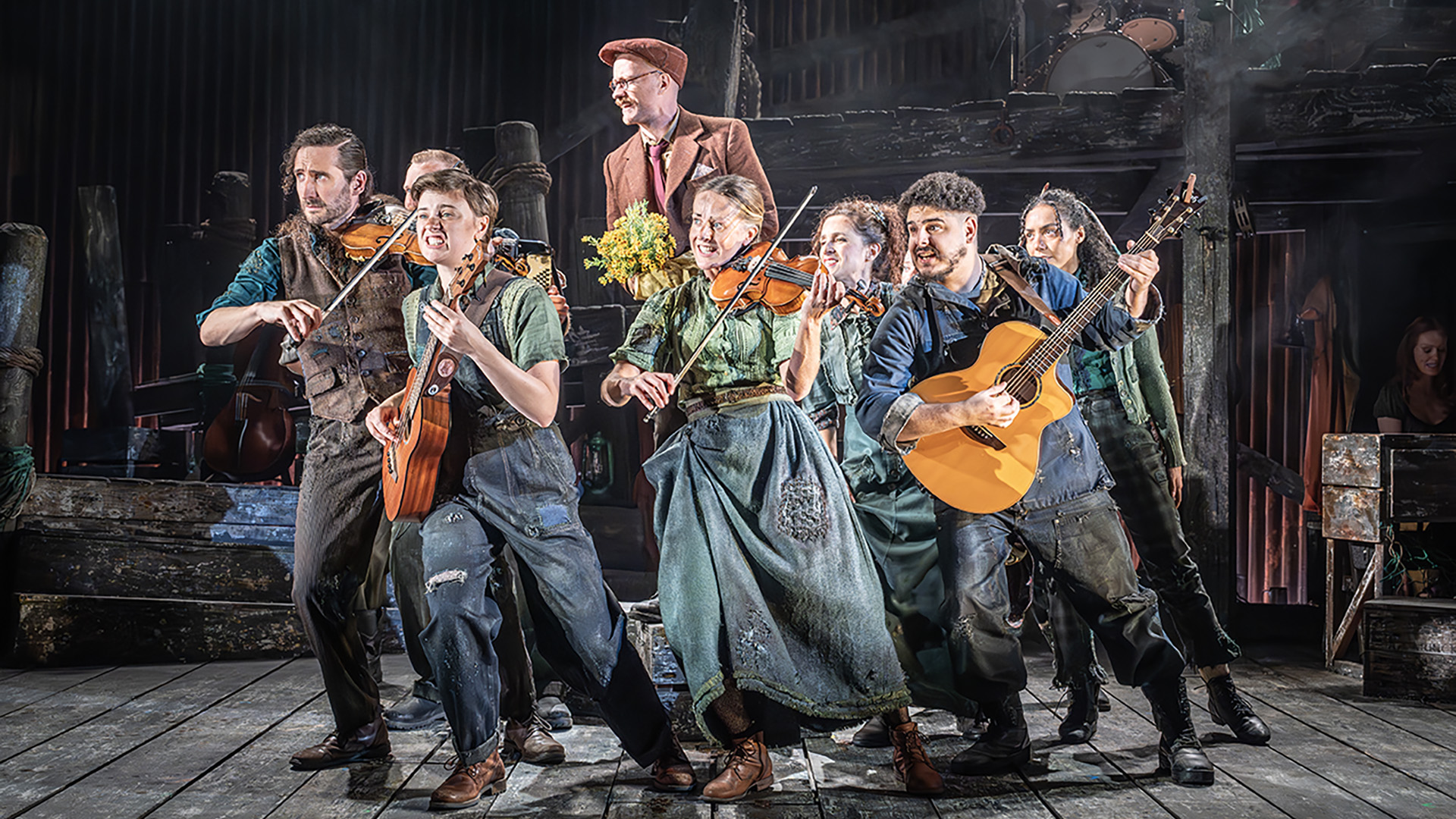 Experience the awe-inspiring journey of man's destiny through time with the retelling of The Curious Case of Benjamin Button. Image courtesy of Marc Brenner. The cast of The Curious Case of Benjamin Button are on stage dancing and playing musical instruments, including violin and acoustic guitar.