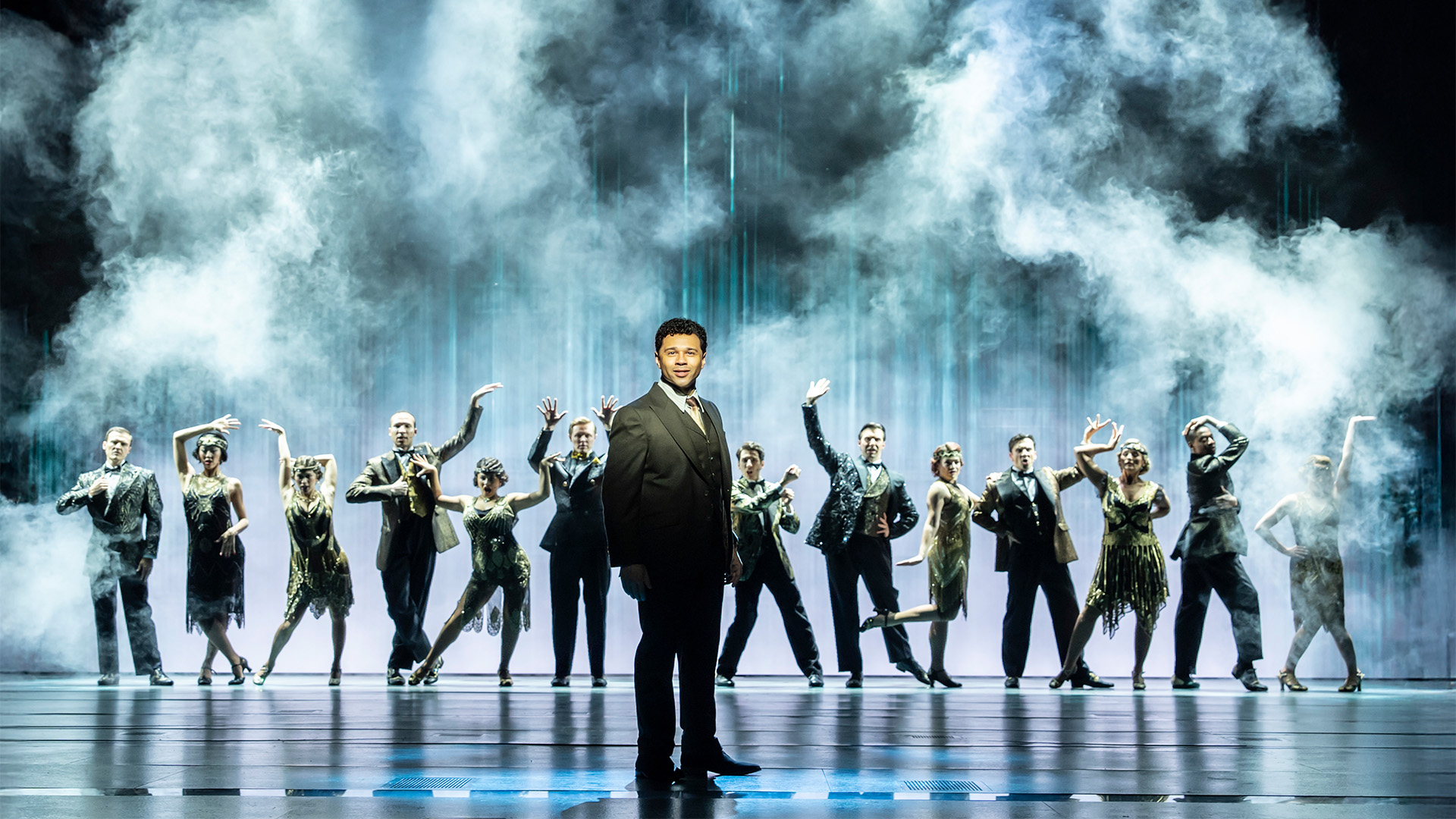 Corbin Bleu as Nick Carraway and the original West End cast of The Great Gatsby. Image courtesy of London Theatre Direct/Johan Persson. Corbin Bleu as Nick Carraway in The Great Gatsby, framed by smoke effects and the cast.