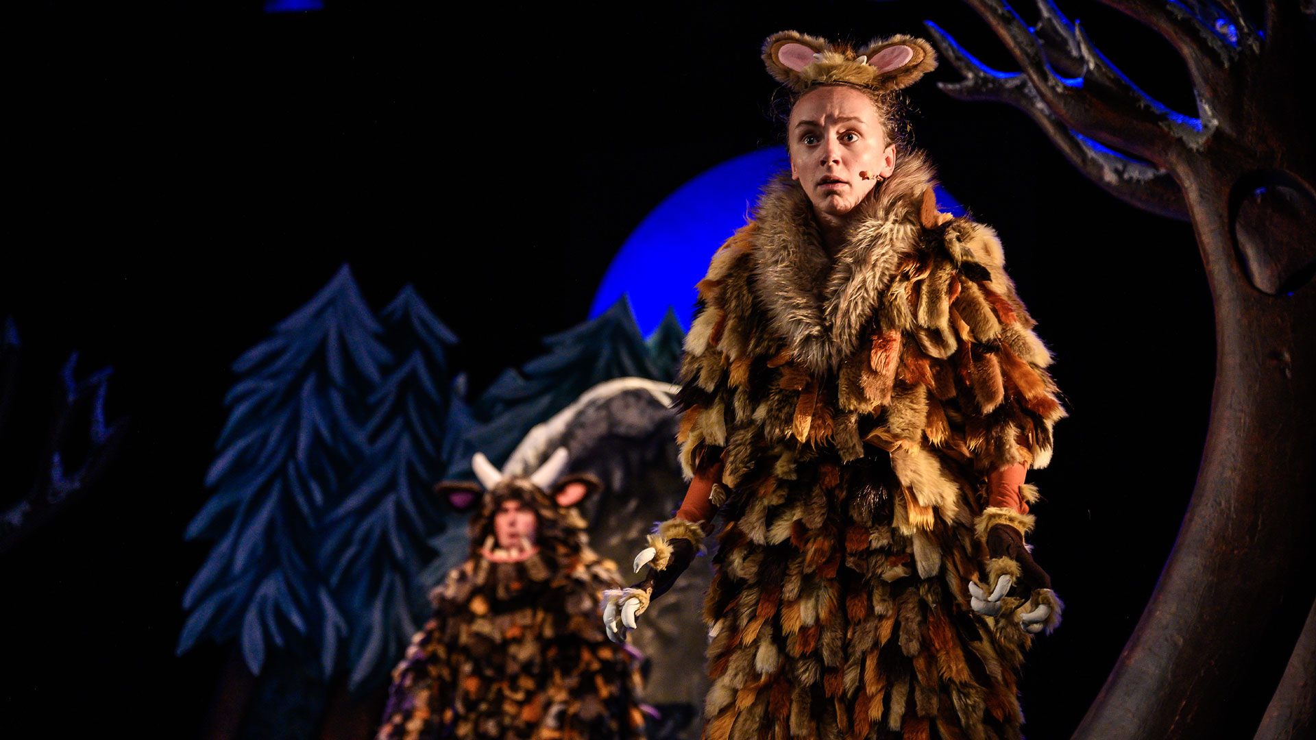 This Christmas, revisit the popular children's book The Gruffalo's Child at the Lyric Theatre in the West End. Image courtesy of Tall Stories. A young actor wearing a long brown fur coat and furry ears is standing on stage as the Gruffalo's Child.