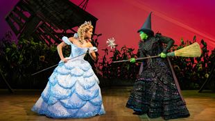 Glinda The Good is wearing a light blue gown and is fighting of Elphaba the Wicked Witch who is branding her broom.