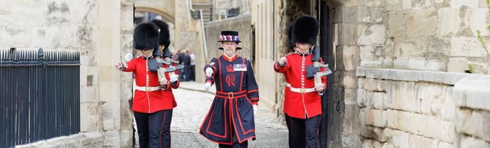 Yeoman warders dressed in black and red march through the tower of london.