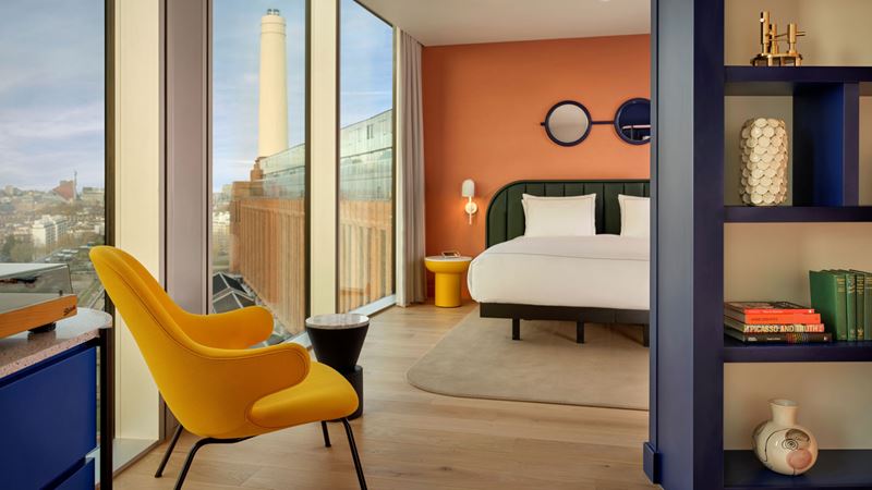 Take in the iconic views of Battersea Power Station from your room. Credit: Matthew Shaw. Image courtesy of art'otel London Battersea Power Station. A bedroom filled with colourful furniture and modern artistic touches with floor-to-ceiling windows showing a view of Battersea Power Station in the background