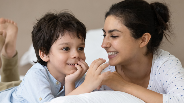 A woman and a child laugh together while lying on a bed.