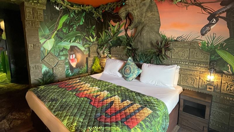 Book the exotic Jumanji-themed room at Chessington Safari Hotel. Credit: Smarts. Image courtesy of Smarts. Jumanji-themed hotel room with logo bed covers and jungle wallpaper featuring images of plants and animals