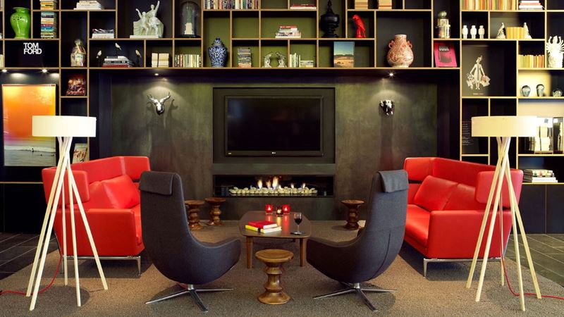 The lounge at citizenM Bankside. Credit: W Communications. Image courtesy of W Communications. Sofas and chairs form a round in the modern lounge with a television, fireplace and bookcase
