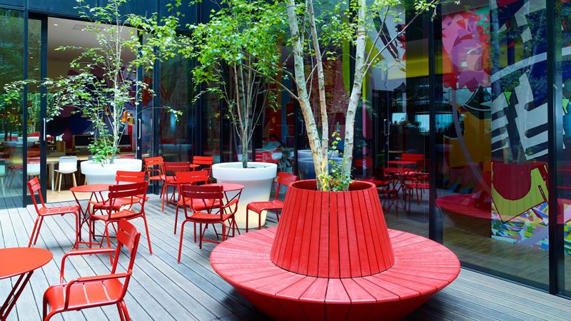 Chill out in one of the many comfortable communal spaces at citizenM Bankside. Credit: citizenM. Image courtesy of citizenM. A photo of the outdoor communal space at Citizen M Bankside with red chairs and tables to sit and relax and trees lining the area with floor-to-ceiling windows looking inside the hotel