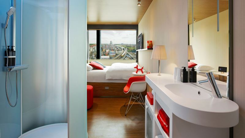 Enjoy a cool and comfortable stay at citizenM Shoreditch with easy access to the quirky area. Credit: citizenM. Image courtesy of citizenM. A photo of a room at Citizen M Shoreditch with a giant window with views of London, a desk and large double bed with coloured lights in the shower that can be controlled with in-room technology