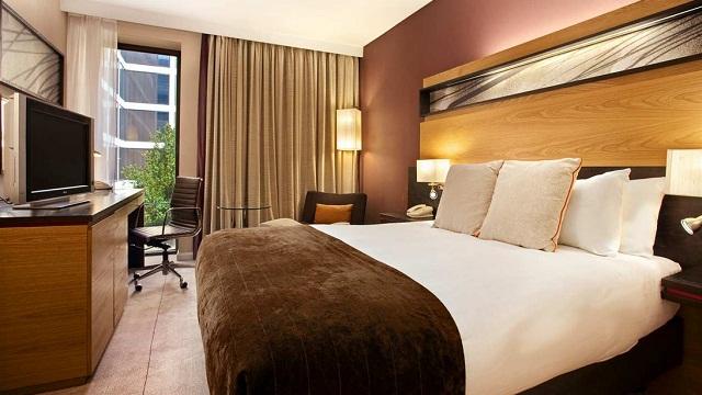 A room at Hilton London Gatwick, with a large bed featuring a brown throw, low-level lighting and a window.